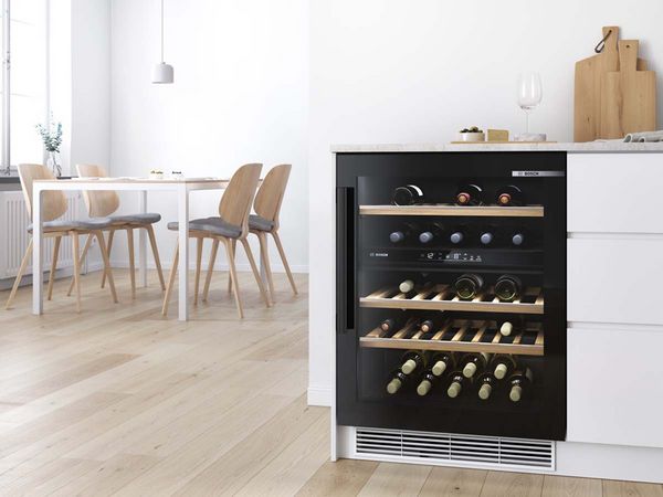 Unterbau-Weinkühler mit zwei Temperaturzonen und ein kleines Esszimmer im skandinavischen Design im Hintergrund.