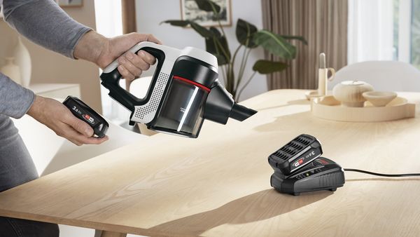 A second Bosch battery charging in fast charger next to an Unlimited handheld vacuum.