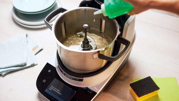 Usuario agregando agua y jabón al recipiente Cookit para una limpieza previa automática