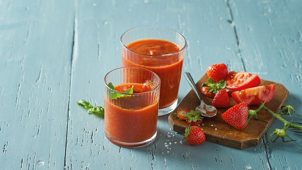 Dva crvena smoothieja u čašama zajedno s jagodama i rajčicama na stolu.