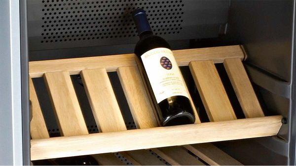 Raudonojo vyno butelis ant medinės lentynos vyno šaldytuvo viduje.