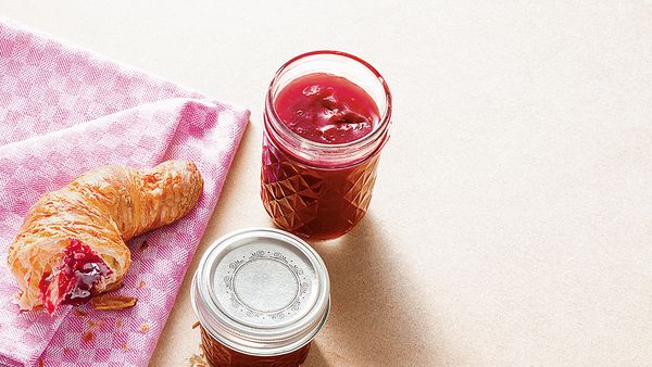 Glass filled with raspberry jam arranged together with a croissant.