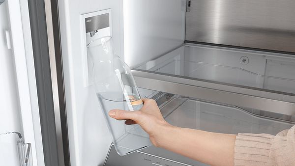 Eine Frau füllt eine Karaffe mit Wasser am Wasserspender in einem French Door Kühlschrank.