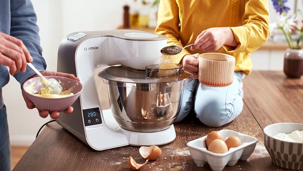 People adding ingredients to the stand mixer's bowl to make a cake.