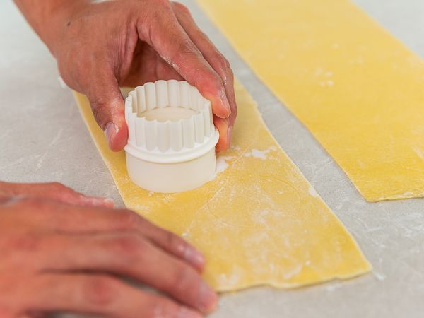 6. Lay two pasta sheets flat on countertop. Dust with excess flour to prevent sticking. Gently make evenly spaced markings with ring mould on one sheet. Brush the same sheet with water. Place 1 tablespoon of filling within each marking. Brush water over the other sheet, lay over first sheet with brushed side down.
