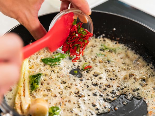 8. Deseed and slice thinly red and green chilli. In lightly heated non-stick pan, fry butter and lime leaves for 2 minutes. Add lemongrass, galangal, remaining chopped garlic and shallots, sliced red and green chilli. Continue frying until soft for about 2 to 3 minutes.