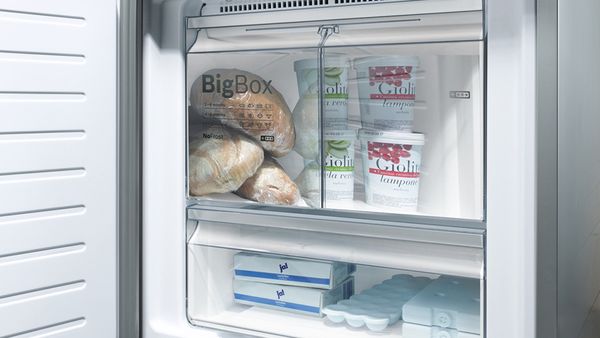 Відкрита морозильна камера з екстравеликою шухлядою, в якій складено хліб і відерця з морозивом.