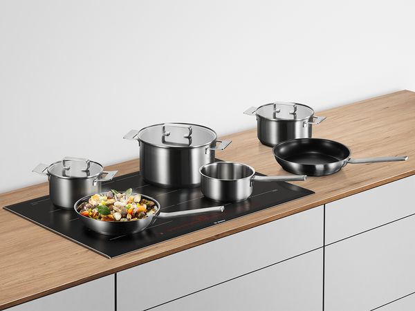 The 6-piece induction cookware set on an induction hob and wood countertop.