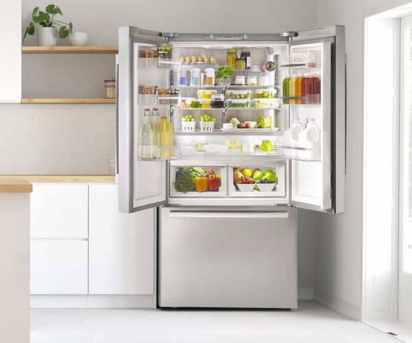 Open stainless steel fridge stocked with fresh produce, drinks and dairy products in a modern kitchen with natural light.