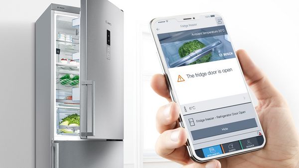 Hand holding a mobile phone with a Home Connect screen alerting that the fridge door is open. 