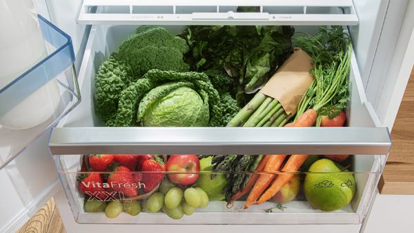 Réfrigérateur-congélateur ouvert avec tiroir, rempli d'ingrédients frais.