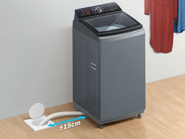 A top load washing machine that shows the drain pipe must lay flat on the ground and not be bent beyond 15 cm.