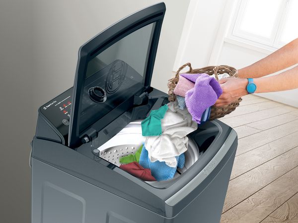 An image showing a person puting clothes in a top load washing machine.