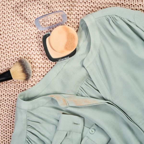 Camicia chiara con macchie di trucco, accanto a pennello e cipria