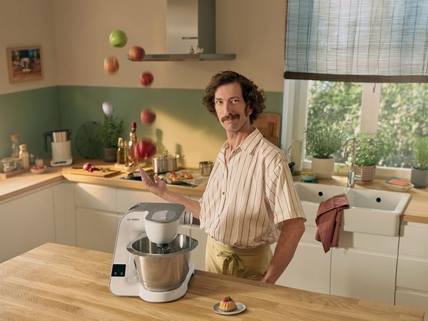 Robot kuchenny MUM5 na blacie. Mężczyzna stojący obok niego, żonglujący owocami.