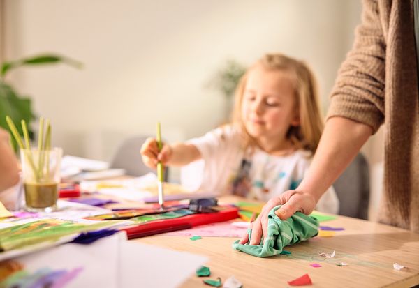 Bambina che dipinge con colori ad acquarello mentre la mamma pulisce il tavolo.