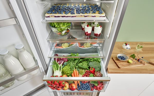 „Bosch“ itin didelio šaldytuvo su šaldikliu detalus vaizdas – jo viduje pilna šviežių maisto produktų, įskaitant kepinį kepimo skardoje, arbūzą, vaisius ir daržoves.