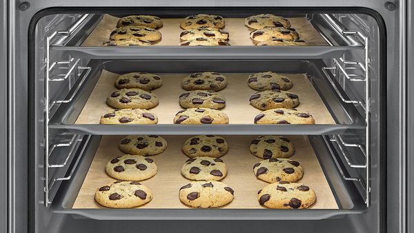 Three trays of chocolate chip cookies baking at once. 