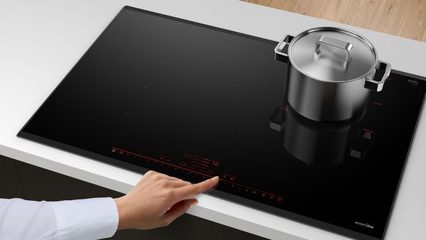 Finger touching the control panel of an induction hob.