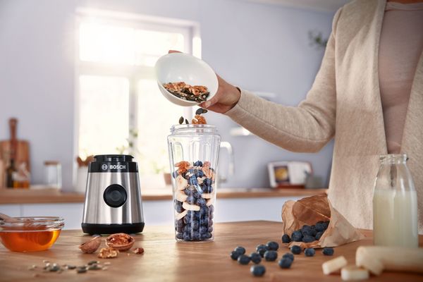 A woman putting fruits and nuts into the Bosch Miniblender VitaPower Series 2.