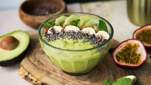 A matcha smoothie bowl with fruits standing on a wooden cutting board.