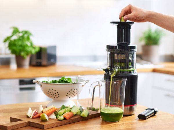 A person is putting a cucumber in the Bosch SlowJuicer VitaExtract and fresh juice coming out of the juicer.