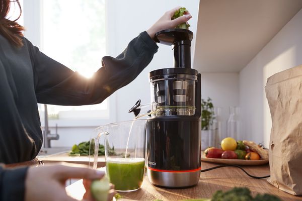 Une femme utilise l'extracteur de jus lent Bosch VitaExtract dans la cuisine pour faire du jus frais.