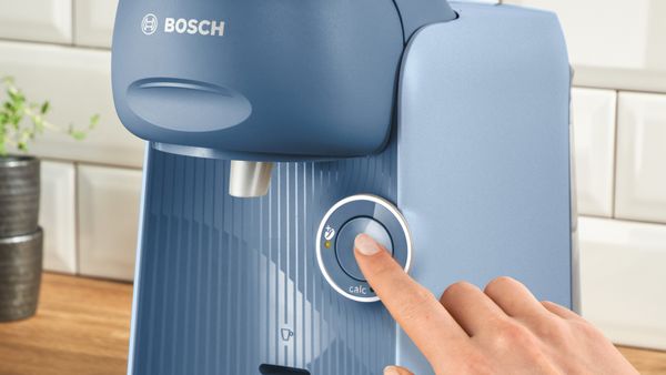 O persoană dă clic pe butonul de pornire al aparatului de cafea TASSIMO FINESSE.