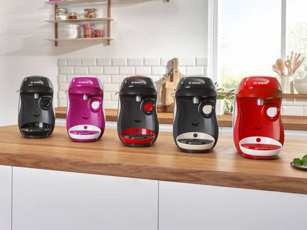 Different colours of the TASSIMO HAPPY coffee machine on a kitchen worktop.