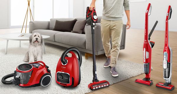 Alle roten Staubsauger der ProAnimal Reihe von Bosch in einem Wohnzimmer aufgereiht. Eine Person saugt den weißen Teppichboden des Wohnzimmers mit einem Akku-Staubsauger Unlimited 8 Gen2 ProAnimal. 