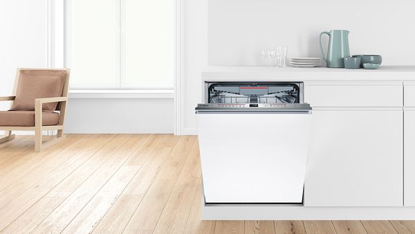 An open built-in dishwasher in a white kitchen.