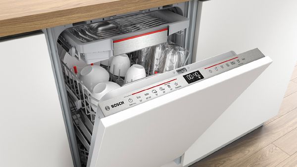 Uma máquina de lavar loiça aberta totalmente integrada num armário branco.