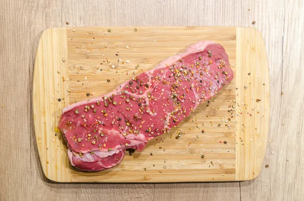 Czerwone mięso z przyprawami leży na drewnianej desce do krojenia.