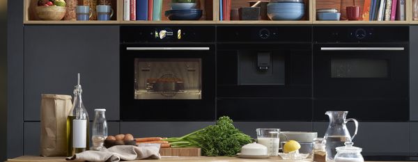 Four intégrable Bosch Série 8, machine à café et four compact derrière un plan de travail de cuisine sur lequel sont posés des ingrédients de cuisson.