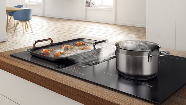 Svetla moderna kuhinja z zrezkom, ki se peče v ponvi na kuhalni plošči.