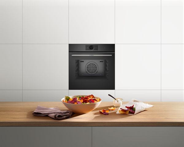Elegante keuken met Serie 8 inbouwoven van Bosch met Air Fry-functie en warmhoudlade. Diverse groenten in de oven. Meer groenten op een snijplank op een werkblad.