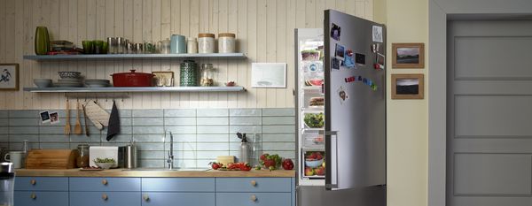 In a kitchen. Bosch refrigerator with an opendoor, filled with fresh food. Letter magnets on the door read "Like a Bosch.”
