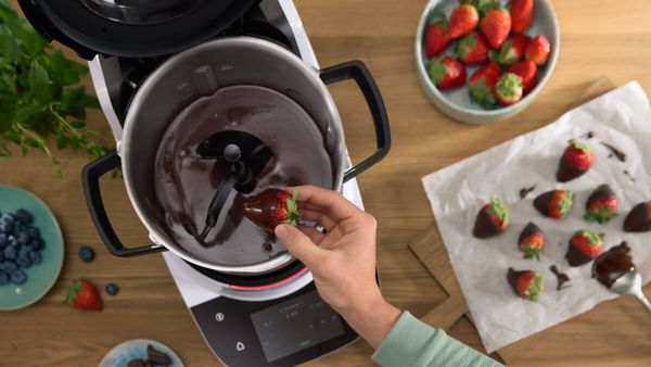 The Cookit is filled with melted chocolate and a strawberry that is being dipped into it. 
