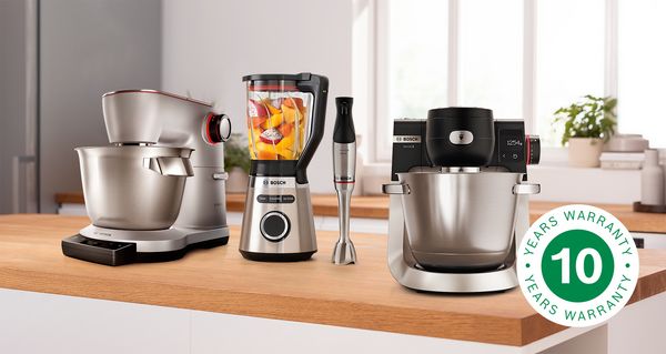 Køkkenmaskine Serie 8 OptiMUM og Serie 6, blender VitaPower Serie 4 og stavblender ErgoMaster Serie 6 står på en bordplade, ved siden af skiltet med 10 års garanti.