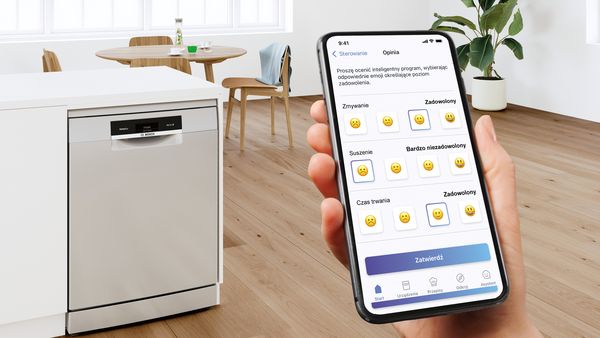 Smartfon z aplikacją Home Connect oraz piekarniki marki Bosch w tle. 