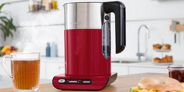 Rýchlovarná kanvica Styline v červeno striebornej farbe, s pohárom čaju.