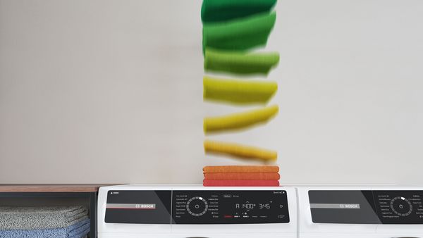 Ein Stapel Handtücher fällt auf die Waschmaschine, wo er als akkurater Stapel landet. Ihre Farben entsprechen den Farben der Energieeffizienzklassen.