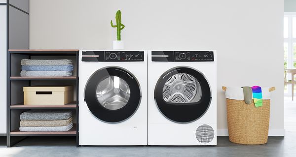 Un lave-linge Bosch Série 8 avec i-DOS est installé à côté d'un sèche-linge pompe à chaleur. Un petit cactus est disposé dessus et fait un signe du pouce.