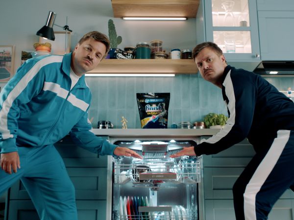 Двама мъже, стоящи пред отворена съдомиялна машина Bosch в кухня с опаковката Finish върху нея, докато търкат купата за лазаня, за да видят колко чисти са съдовете.