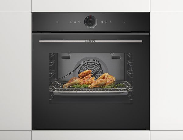 A crispy chicken in front of a Bosch oven in a modern white kitchen.