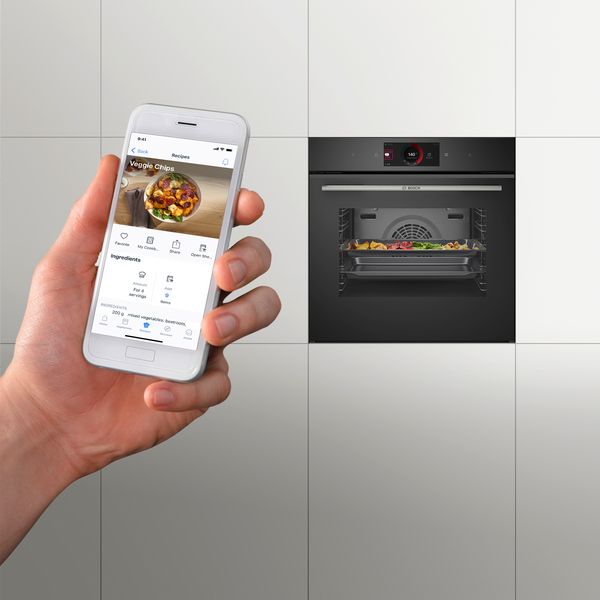 De Home Connect app op een smartphone. Een slimme oven op de achtergrond.