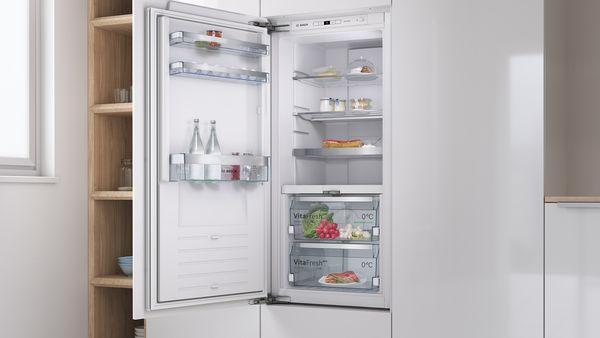 Bosch Einbau-Kühlschrank ohne Gefrierfach mit geöffneter Tür, gefüllt mit Lebensmitteln und Wasserflaschen in einer modernen Einbauküche