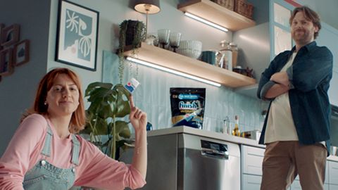 A man and woman in front of their dishwasher by a finish tablet packet