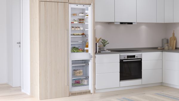 Eine Bosch Einbau-Kühl-Gefrierkombination mit Gefrierbereich unten mit geöffneten Türen in einer modernen Küche in Weiß und Holz
