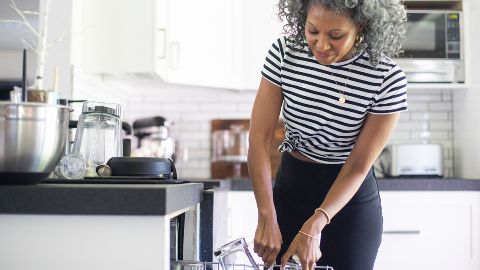 Woman in striped shirt loading dishwasher with dishes.